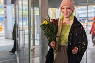 Oodi's ten millionth visitor Sonja in front of Oodi's doors with a bouquet of flowers in her hand.