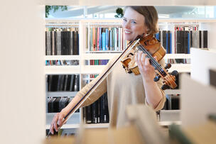 A woman plays the violin in front of the bookshelves in the library