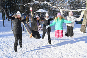 A teacher and four students jump into the air at the Tuhkimo playground in the wintertime.