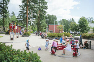 Kesäpäivä Myllynsiiven leikkipuistossa. Lapsia juoksee pihalla. Lapsia pienen karusellin kyydissä.