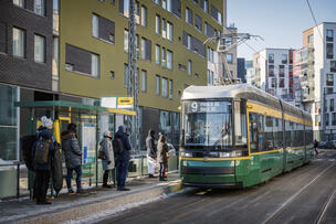 Raitiovaunu on pysähtymässä pysäkille, jossa odottaa ihmisiä.