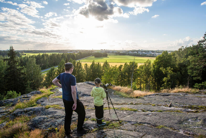 Mies ja poika katselevat Hallainvuoren kallioilta Viikin peltojen yli länteen.