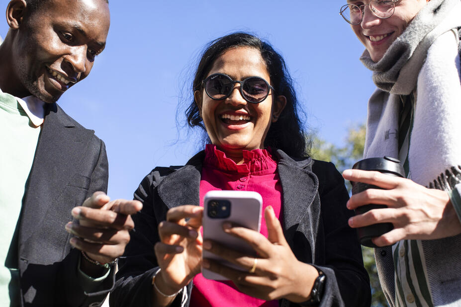 Kolme ihmistä katsoo yhdessä kännykkää ja hymyilee.