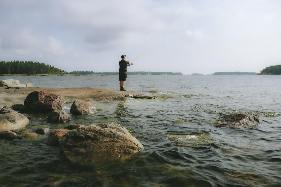 Kalastaja vavan kanssa kallion päällä meren äärellä.