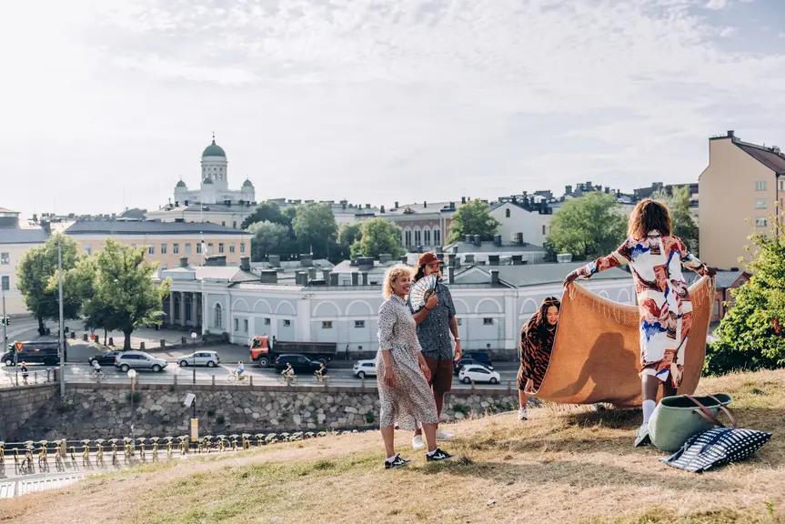 Joukko ihmisiä piknikillä, Helsingin tuomiokirkko maisemana taustalla.